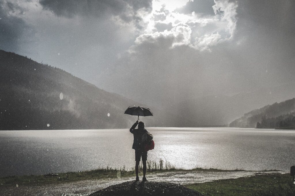 雨の中に傘をさして立つ女性の画像